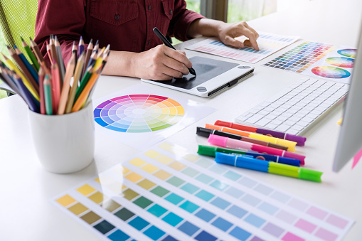 Image of female creative graphic designer working on color selection and drawing on graphics tablet at workplace.