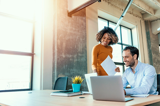 We already have great results! Young beautiful woman working, discussing something with her coworker while standing at office.